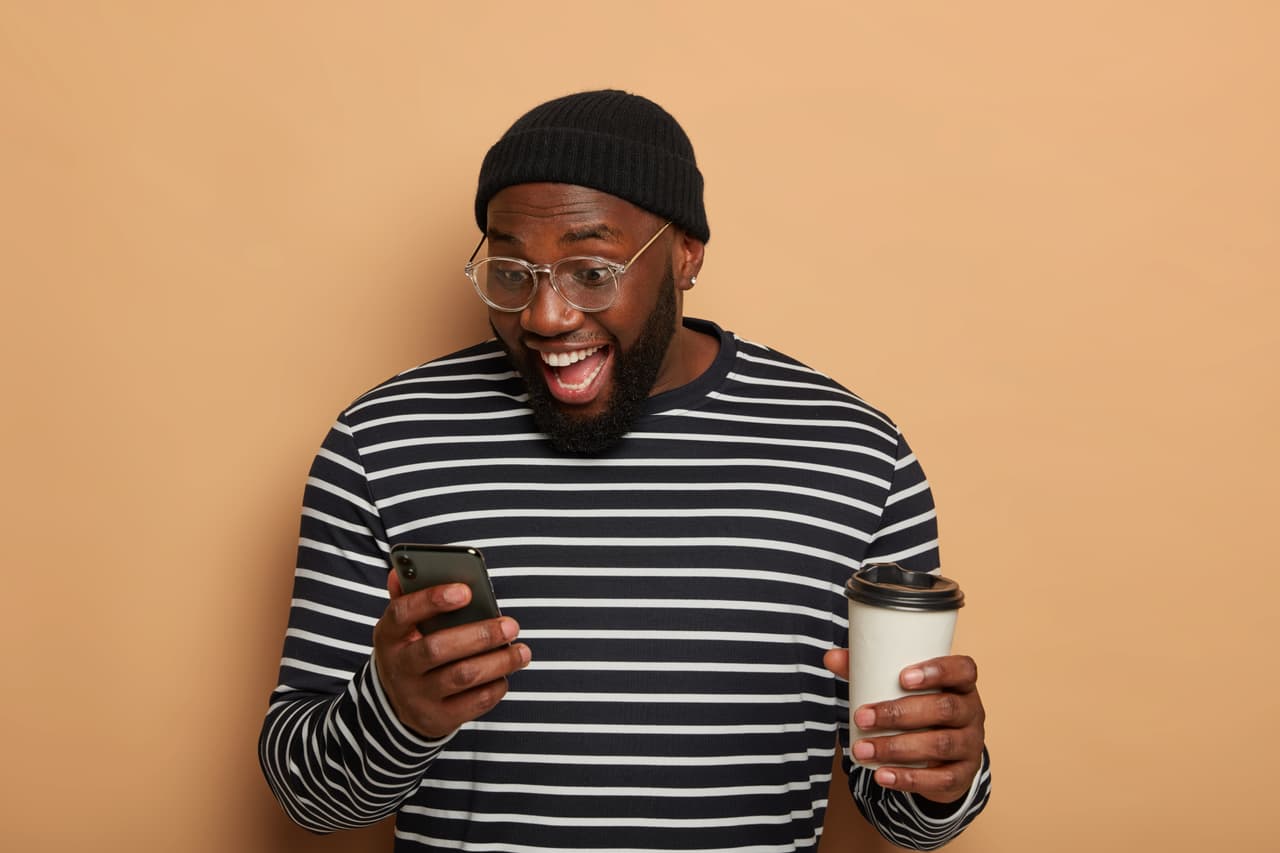 Team member smiling at his phone with a coffee in hand